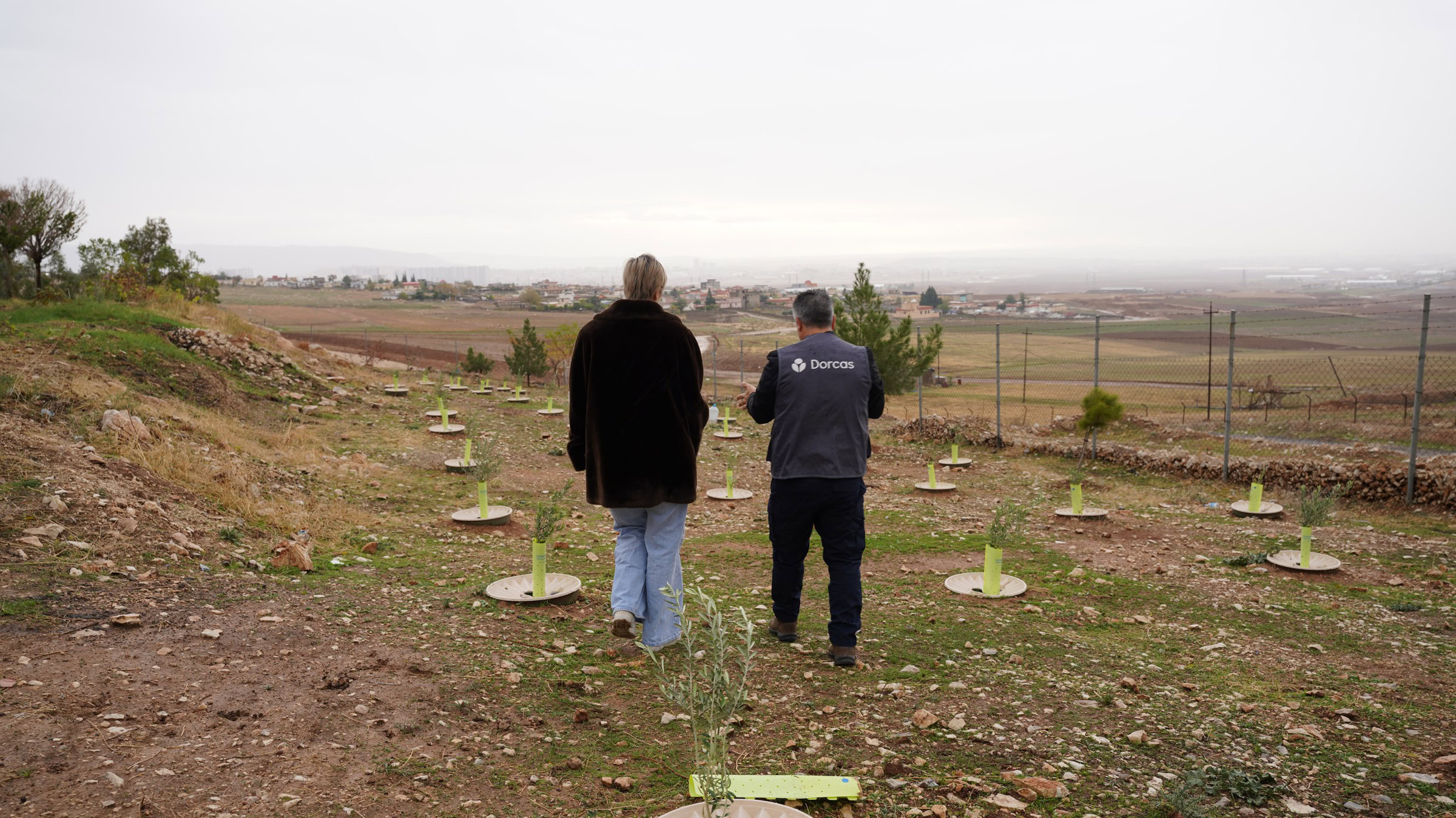 Twee mannen wandelen over een open veld met jonge bomen, met uitzicht op een landbouwgebied op de achtergrond, symboliserend het opbouwen van zakelijke relaties en netwerken.