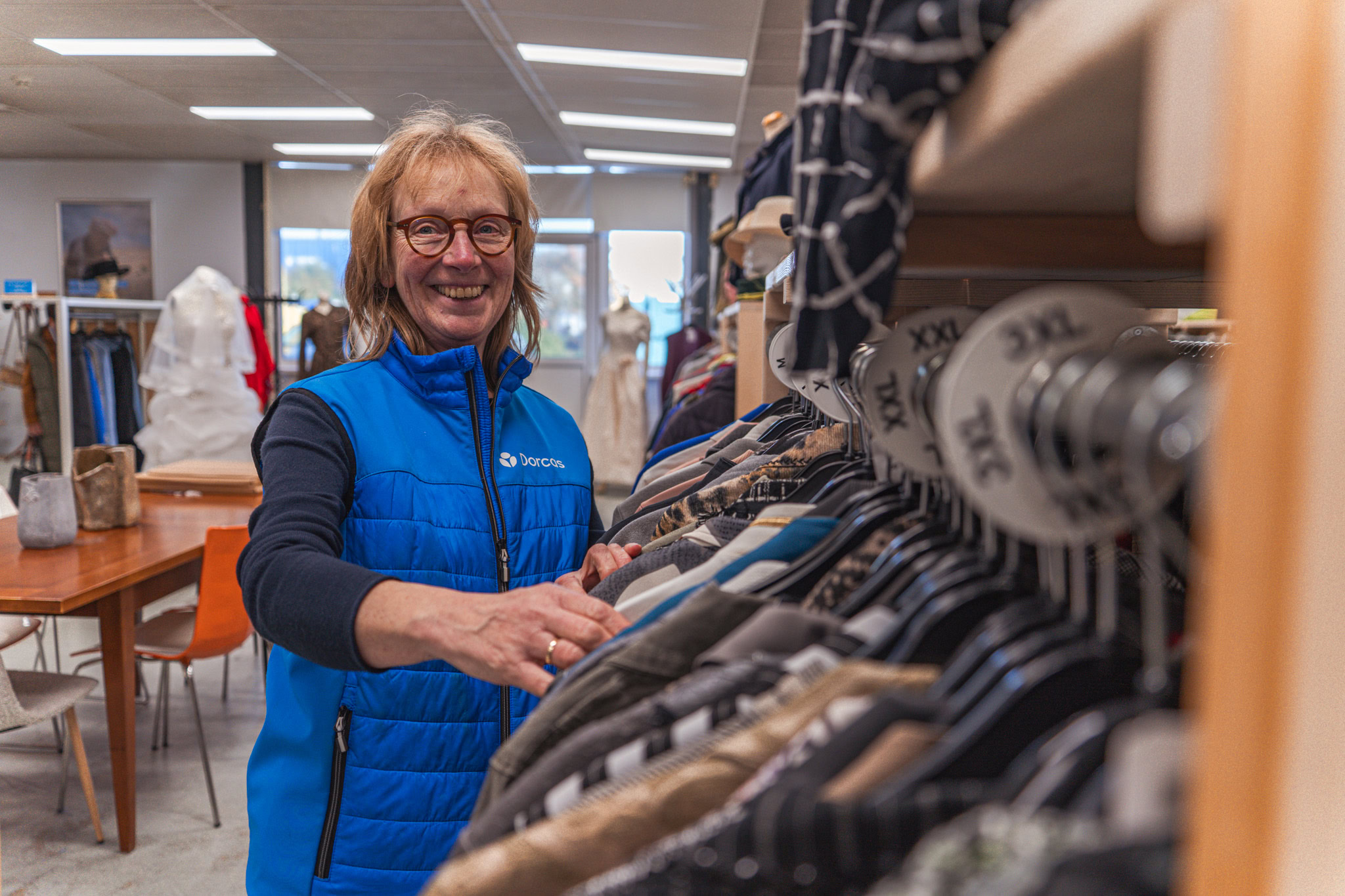 Dame met winkelmedewerker in Doris winkel, die kleding uitkiest op een kledingrek met diverse outfits en accessoires in een heldere winkelruimte.