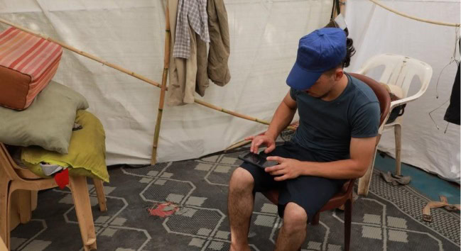 Een jonge man zit in een tent, gebruikmakend van een tablet