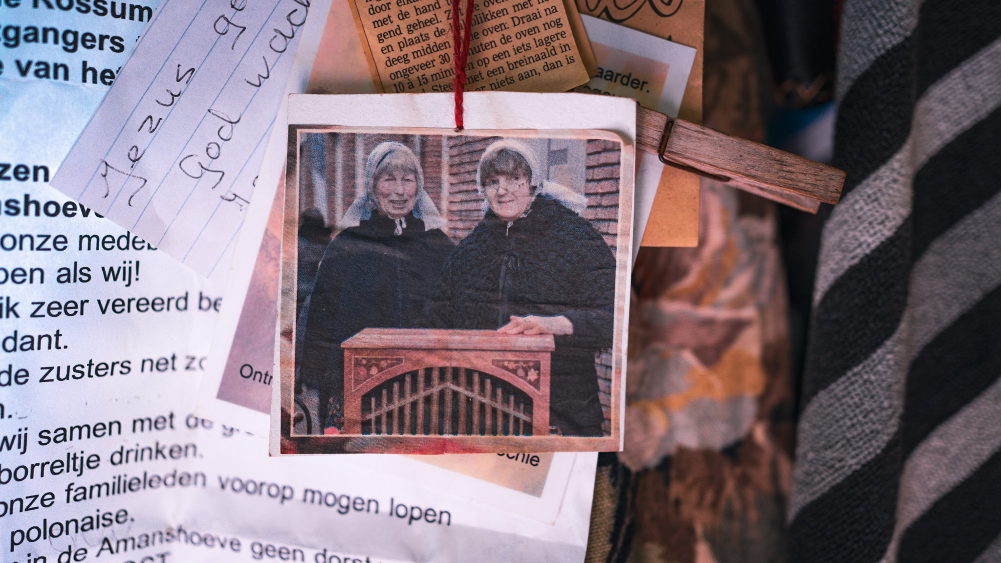 Twee vrouwen in gewaad poseren achter een houten object bij een herdenkings- of gedenkplek.