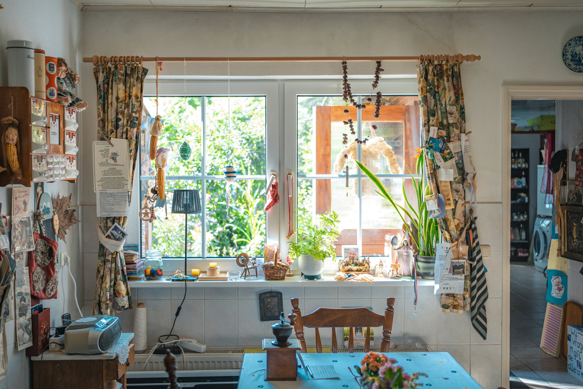 Gezellige keuken met veel planten, decoraties en natuurlijke lichtinval, ideaal voor huiselijke momenten en knusse sfeer.