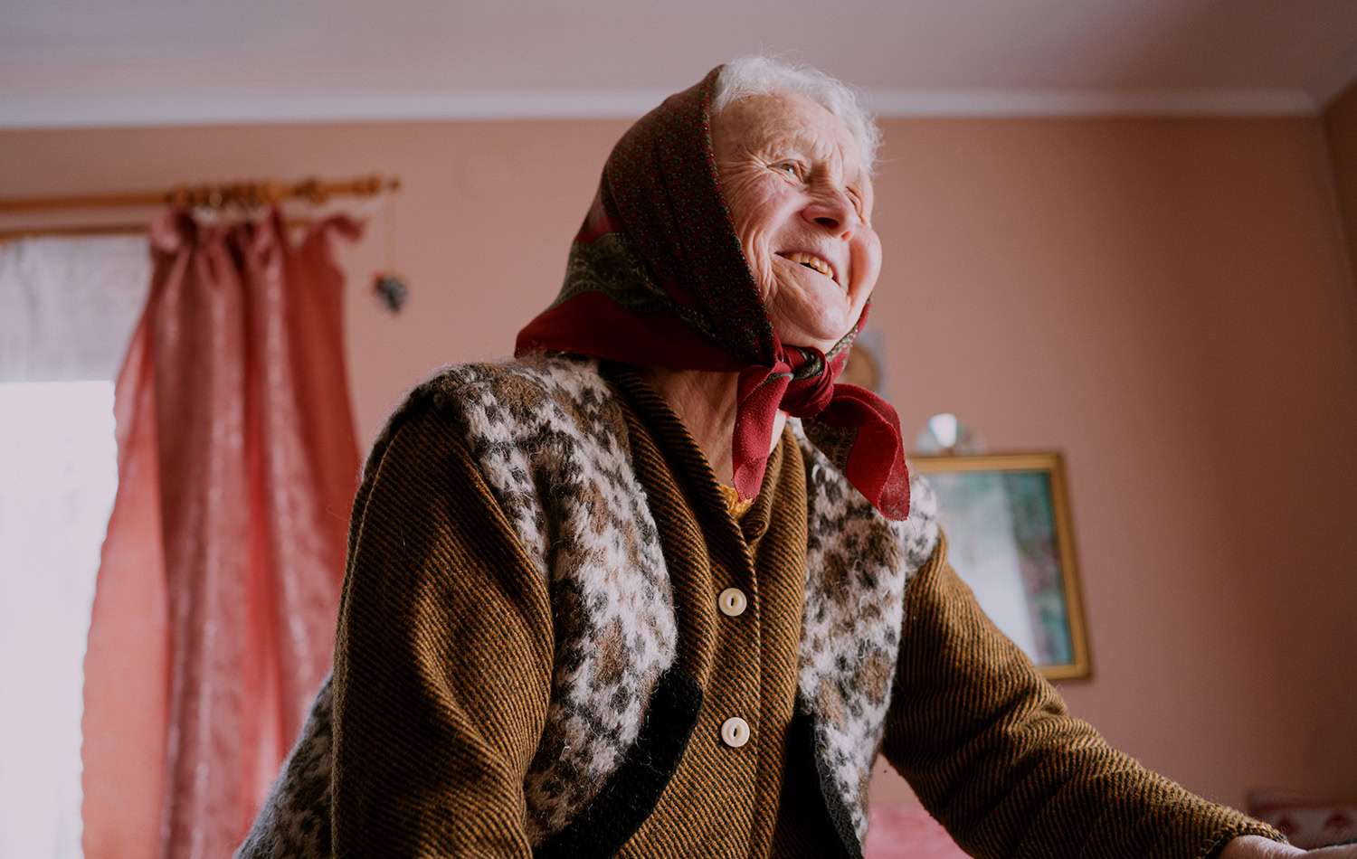 Oudere vrouw met hoofddoek lacht tijdens het sociaal contact, binnen in huis.