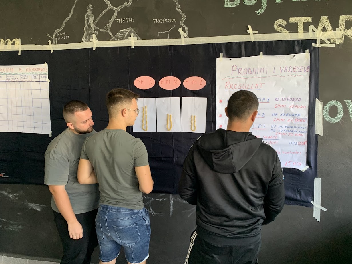 Drie mensen bekijken een informatiebord en posters over tips en regelgeving bij een georganiseerde activiteit of workshop.