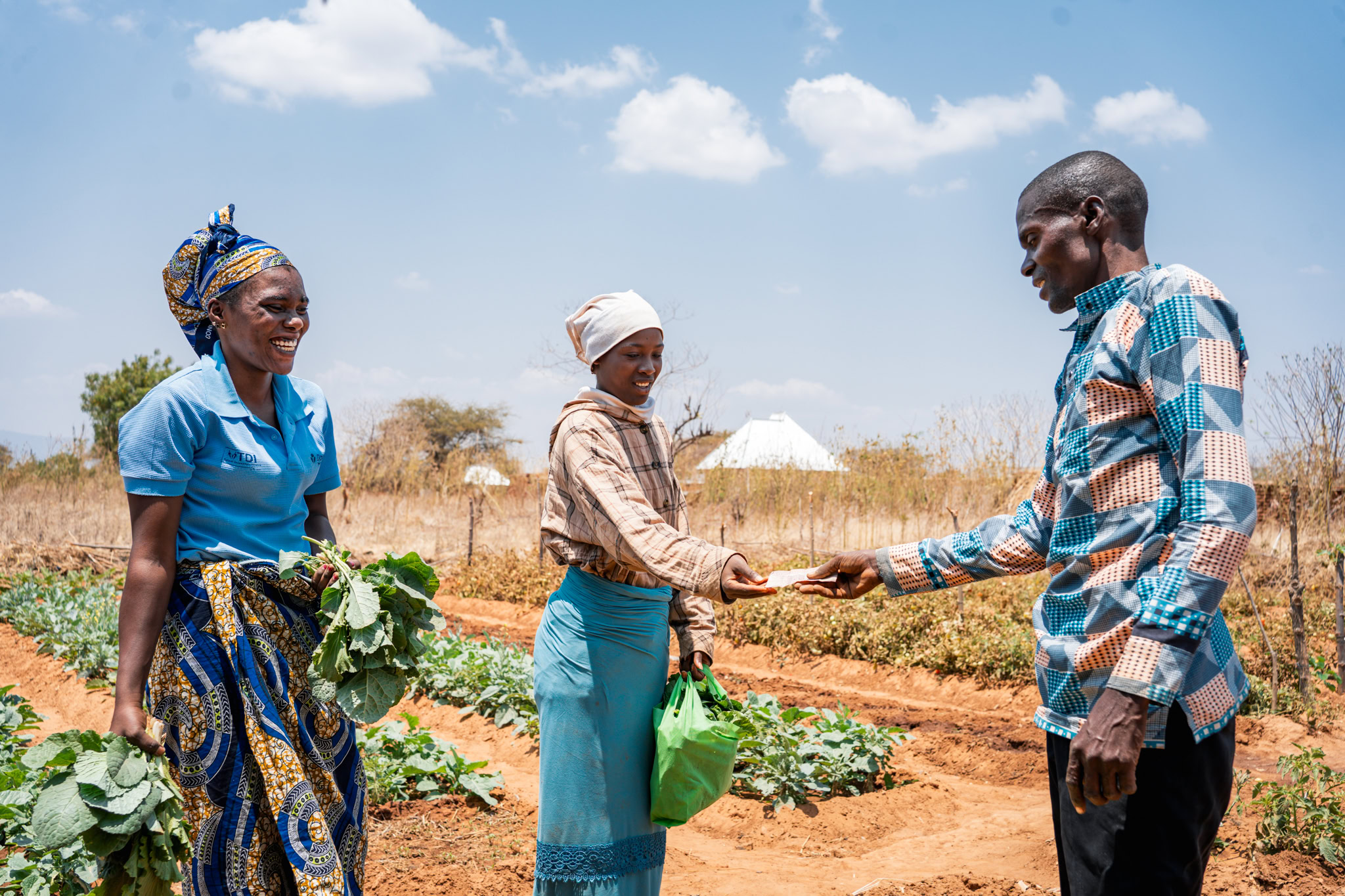 Drie mensen die in een moestuin werken, waarbij een man een schenking ontvangt van een vrouw, onder begeleiding van een vrouw met gewassen in handen.