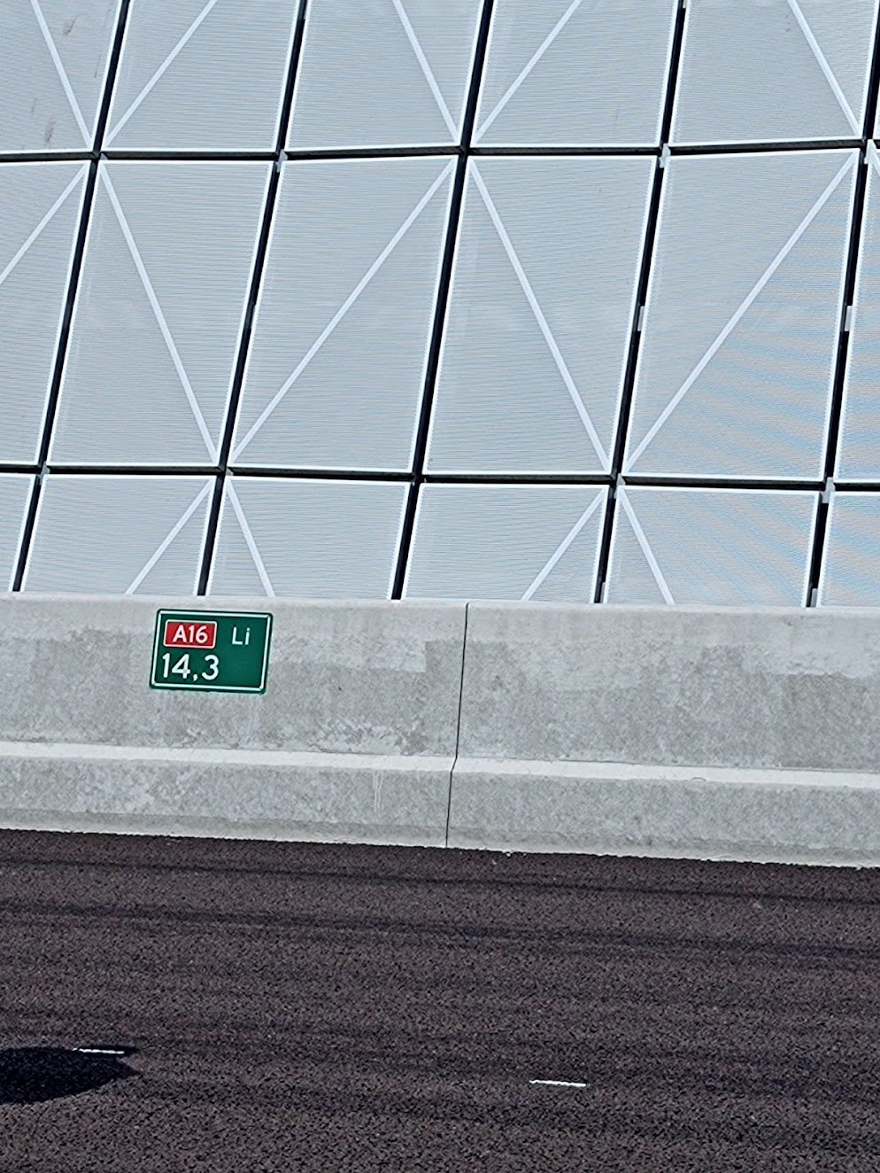 Modern gebouw met geometrische gevelpanelen ondergrond met snelwegbordje A16 Li 14,3 meter.